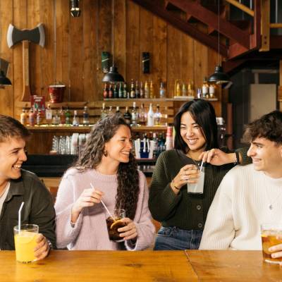 Happy group of young friends, with drinks, enjoying a party in a bar. Four friends hanging out in a bar.